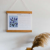 zoomed out photo of liturgical calendar hanging on wall next to vase 