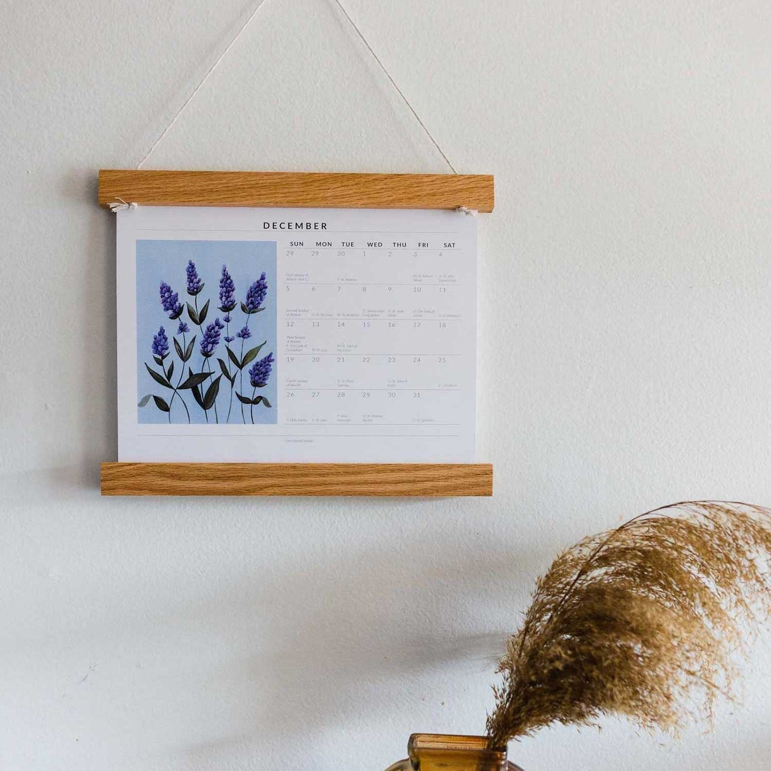 zoomed out photo of liturgical calendar hanging on wall next to vase 