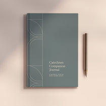 Catechism Companion Journal next to metal pen on light brown background 
